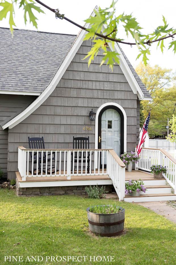 black rockers, charm, cottage style, cottage style curb appeal, cottage style front yard, curb appeal, deck, entryway, flowers, front door, Front Porch, front yard, Home Accents, lantern, outdoor decor, Outdoor Entryway, outdoor lighting, outdoor plants, outdoor seating, Outdoors, paint, patio, Planters, Plants, Porch, round storm door, spring, stain, stone, storm door