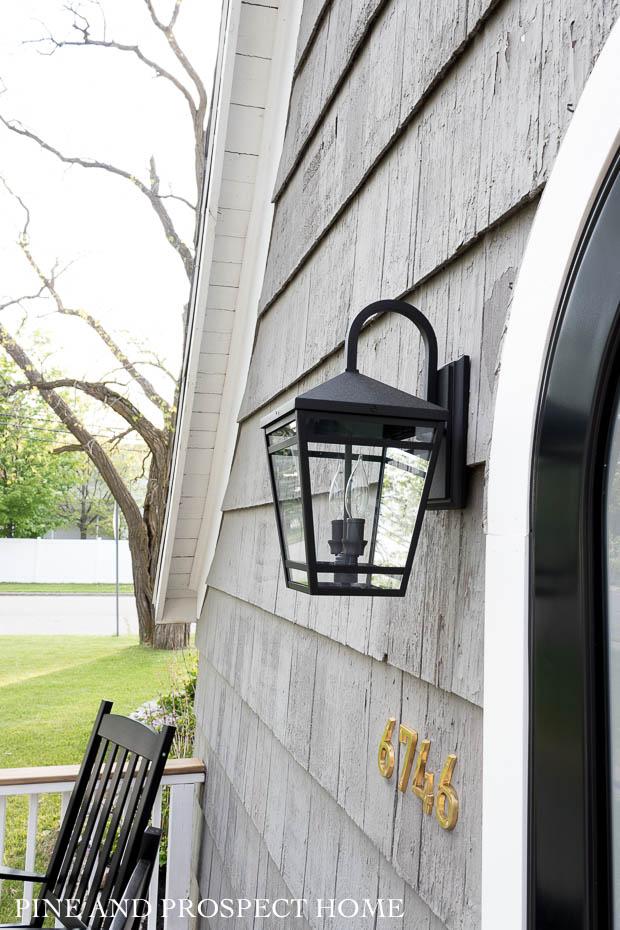 black rockers, charm, cottage style, cottage style curb appeal, cottage style front yard, curb appeal, deck, entryway, flowers, front door, Front Porch, front yard, Home Accents, lantern, outdoor decor, Outdoor Entryway, outdoor lighting, outdoor plants, outdoor seating, Outdoors, paint, patio, Planters, Plants, Porch, round storm door, spring, stain, stone, storm door