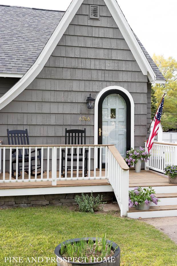 black rockers, charm, cottage style, cottage style curb appeal, cottage style front yard, curb appeal, deck, entryway, flowers, front door, Front Porch, front yard, Home Accents, lantern, outdoor decor, Outdoor Entryway, outdoor lighting, outdoor plants, outdoor seating, Outdoors, paint, patio, Planters, Plants, Porch, round storm door, spring, stain, stone, storm door
