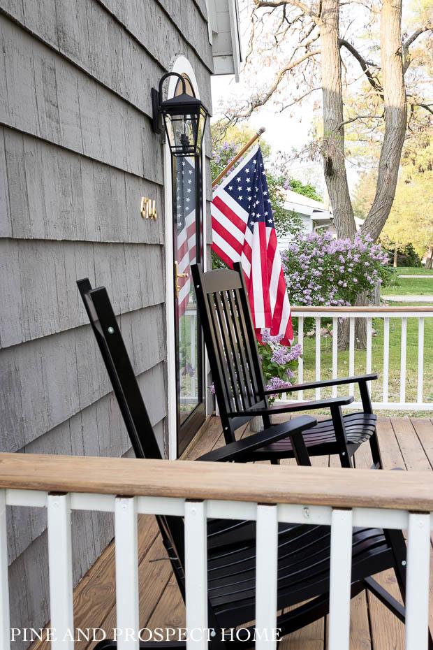 black rockers, charm, cottage style, cottage style curb appeal, cottage style front yard, curb appeal, deck, entryway, flowers, front door, Front Porch, front yard, Home Accents, lantern, outdoor decor, Outdoor Entryway, outdoor lighting, outdoor plants, outdoor seating, Outdoors, paint, patio, Planters, Plants, Porch, round storm door, spring, stain, stone, storm door